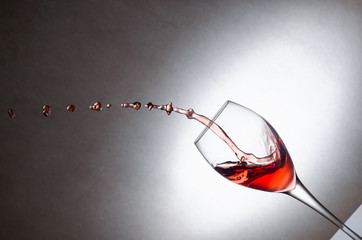 Glass with splashes, drops of red wine on a white background. Freezing liquids in motion. Glass of...