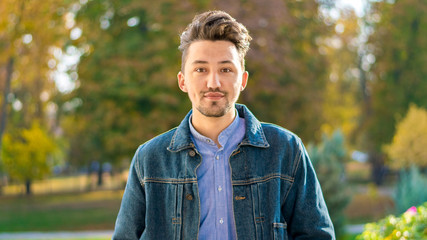 Handsome young man looking at the camera. Portrait of a confident and successful young man with a denim jacket and blue shirt outside. Happy guy smiling