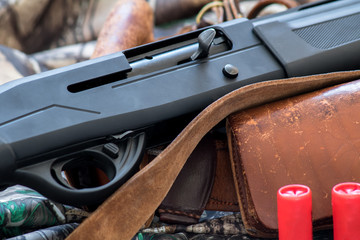 close-up view of black shotgun old leather cartridge belt and red shotgun shells on the camouflage background