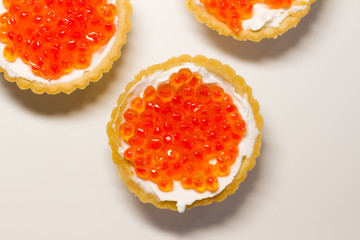 three tartlets with cream cheese and red caviar on a white background. the concept of a delicious Breakfast, buffet and snack. seafood dish. the view from the top. space for text.