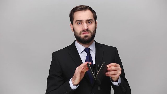 Sad bearded young business man in classic black suit shirt isolated on grey background studio. Achievement career wealth business concept. Mock up copy space. Hold empty wallet without money, no cash