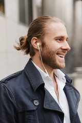 Image of young businessman wearing earphones walking on city street