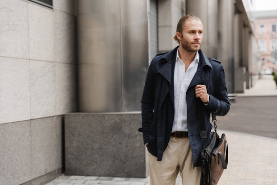 Image of handsome young confident businessman walking on city street