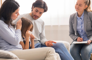 Caring parents comforting their little crying daughter at children psychologist's office