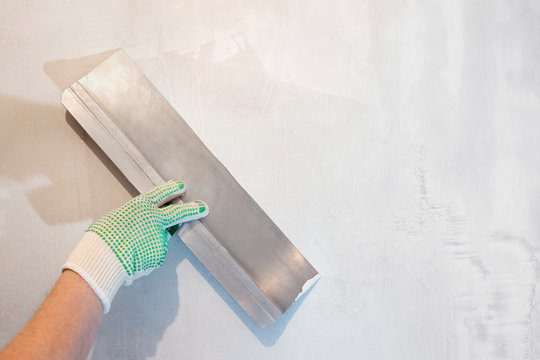 Hand holding a spatula. Tools, plaster wall.