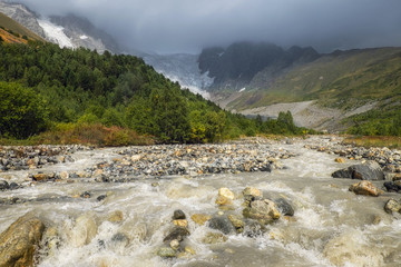 Gloomy dramatic landscape with mountain river Adishi, forest and glacier on a sunny day with clouds