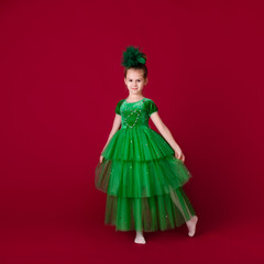 Beautiful little girl princess dancing in luxury green dress isolated on red background. Carnival party with costumes