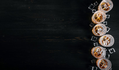 many glasses of whiskey with ice on a black table