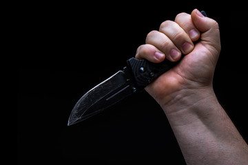 Male hand with a knife on a black background.