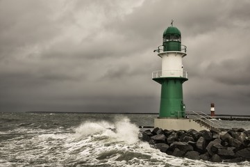 Lighthouse on the pier in Warnemuende during storm the waves break on the pier - Baltic Sea in Germany