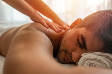Fototapeta na wymiar Masseur doing back massage on man body in the spa salon. Beauty treatment concept. Girl in a T-shirt doing a massage to a guy. Candles in the foreground. Man lying on the table on a white background.