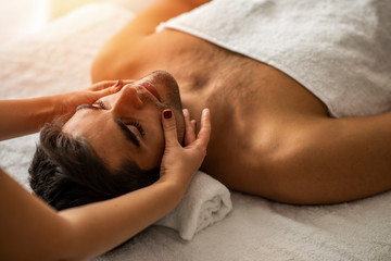 Male beauty - man receiving facial massage at luxury spa. Handsome guy, face massage. Hands of a masseuse working. Handsome man at the spa getting a facial. Man getting a massage at the healthspa