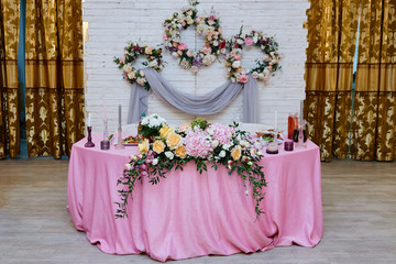 Wedding presidium in restaurant, copy space. Banquet table for newlyweds with flowers, greenery, candles and pink cloth. Lush floral arrangement. Luxury wedding decor