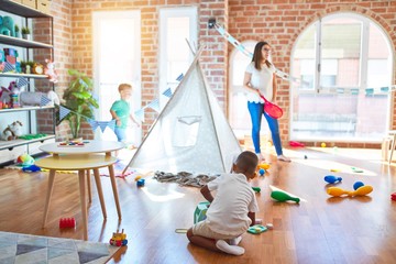 Young beautiful teacher and toddlers playing around lots of toys at kindergarten