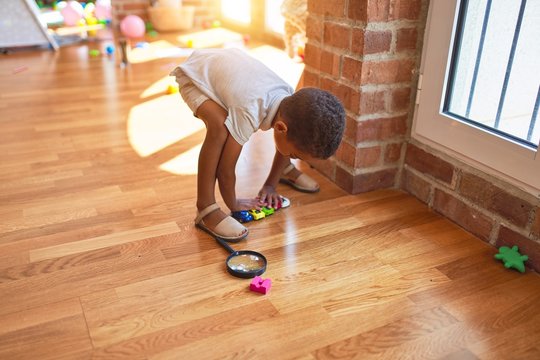 Beautiful african american toddler playing with cars around lots of toys at kindergarten