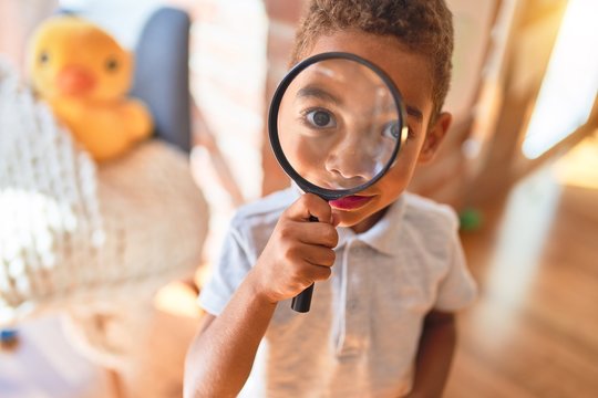 Beautiful african american toddler playing with loupe at kindergarten