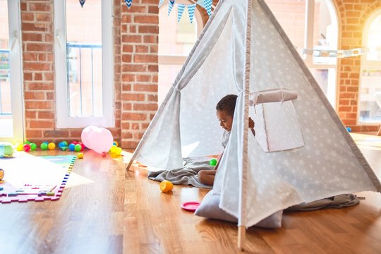 Beautiful african american toddler playing inside tipi smiling at kindergarten