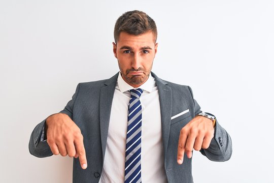 Young handsome business man wearing suit and tie over isolated background Pointing down looking sad and upset, indicating direction with fingers, unhappy and depressed.