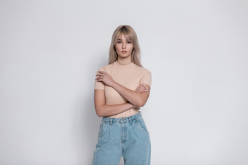 Young amazing woman in a fashionable shirt in vintage blue jeans stands near a modern white wall...