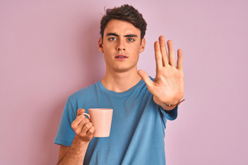 Teenager boy drinking a cup of coffee over isolated pink background with open hand doing stop sign with serious and confident expression, defense gesture