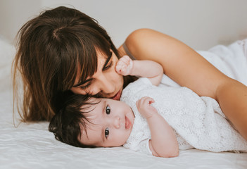 baby lying in bed next to her mom who is hugging her - family concept
