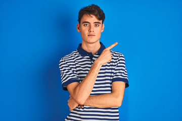 Teenager boy wearing casual t-shirt standing over blue isolated background Pointing with hand...