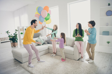 Full body photo of energetic fun people celebrate family day dad daddy give present gift surprise his three small schoolgirls mom mommy sit cozy couch clap hands enjoy fest in house room