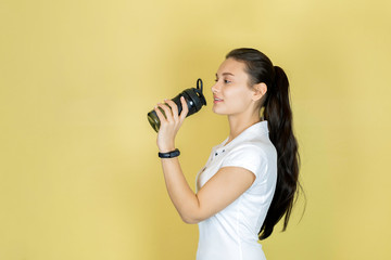 Obraz premium Beautiful young woman the brunette in white t-shirt with a fitness shaker drinking water. Sport fitness. copy space