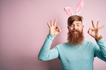 Hipster Irish man with beard wearing easter rabbit ears over isolated pink background relax and smiling with eyes closed doing meditation gesture with fingers. Yoga concept.