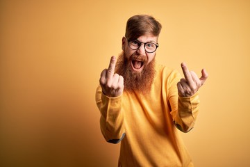 Handsome Irish redhead man with beard wearing glasses over yellow isolated background Showing...