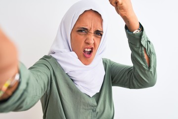 Young Arab woman wearing hijab taking selfie photo over isolated background annoyed and frustrated shouting with anger, crazy and yelling with raised hand, anger concept