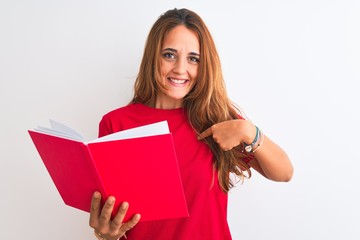 Young beautiful redhead woman reading a red book over isolated background with surprise face pointing finger to himself