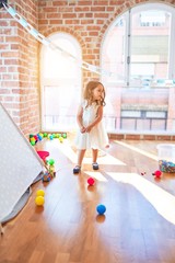 Adorable blonde toddler playing with train toy around lots of toys at kindergarten