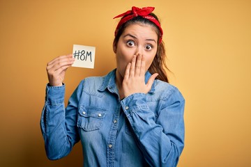 Young beautiful brunette woman celebrating 8th march womens day holding reminder paper cover mouth...