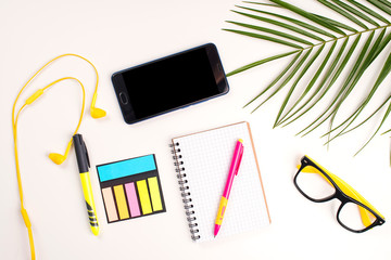 Work desk with open notebook, glasses, phone, headphones and palm leaf, top view. Summer mockup, flat lay. Minimal style.