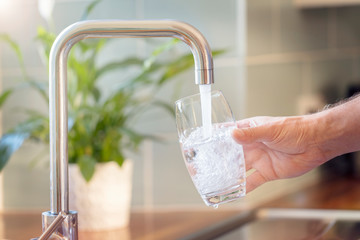 Filling up a glass with drinking water from kitchen tap - obrazy, fototapety, plakaty