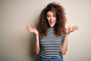 Young beautiful woman with curly hair and piercing wearing casual striped t-shirt celebrating crazy and amazed for success with arms raised and open eyes screaming excited. Winner concept