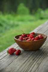 Red fresh strawberries in a old rustic wooden bowl. Raw food on a green background. 
