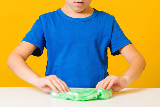 Cute boy playing with slime on a white desk. Hobby and leisure for kid. Art class, creative lessons.