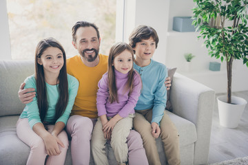 Positive cheerful family dad daddy sit couch hug his three lovely kids schoolboy schoolgirl younger...