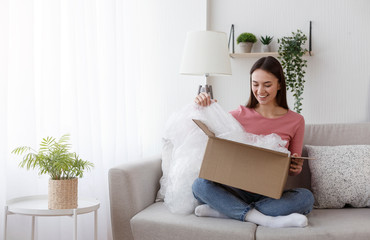 Excited young woman unwrapping parcel, buying goods via internet