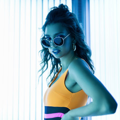 Stylish sexy young woman with curly hair in trendy sunglasses in a colored stylish swimsuit...