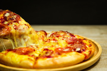 Very cheesy pizza slice in hand.Hot pizza slice with melting cheese on a rustic wooden table.