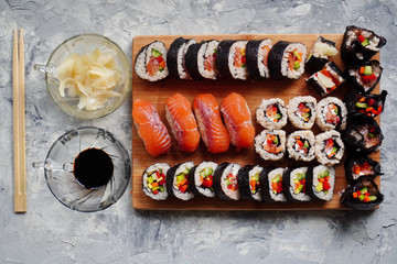 Set of homemade sushi or rolls with salmon, sesame seeds serving on a wood serving board on grey background with ginger, cooking at home.