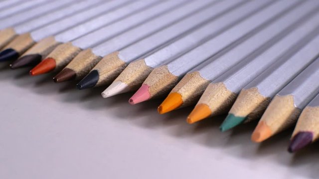 Camera moves above rows of colored pencils on white background. Endless coloring pencils arranged in row. Colored Pencils Background.