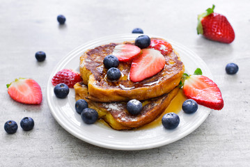 Delicious french toast with fresh fruits and maple sirup. Tasty breakfast scene or dessert with toast, strawberries, blueberries and powdered sugar.