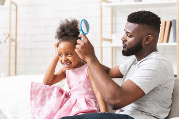 Handsome young man combing his little daughter hair
