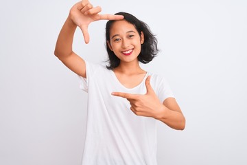 Young chinese woman wearing casual t-shirt standing over isolated white background smiling making frame with hands and fingers with happy face. Creativity and photography concept.