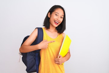 Young chinese student woman wearing backpack holding book over isolated white background very happy pointing with hand and finger