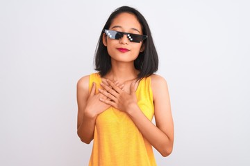 Young beautiful chinese woman wearing thug life sunglasses over isolated white background smiling with hands on chest with closed eyes and grateful gesture on face. Health concept.